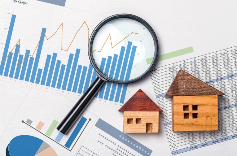 magnifying glass and wooden house models on top of graphs home inspection