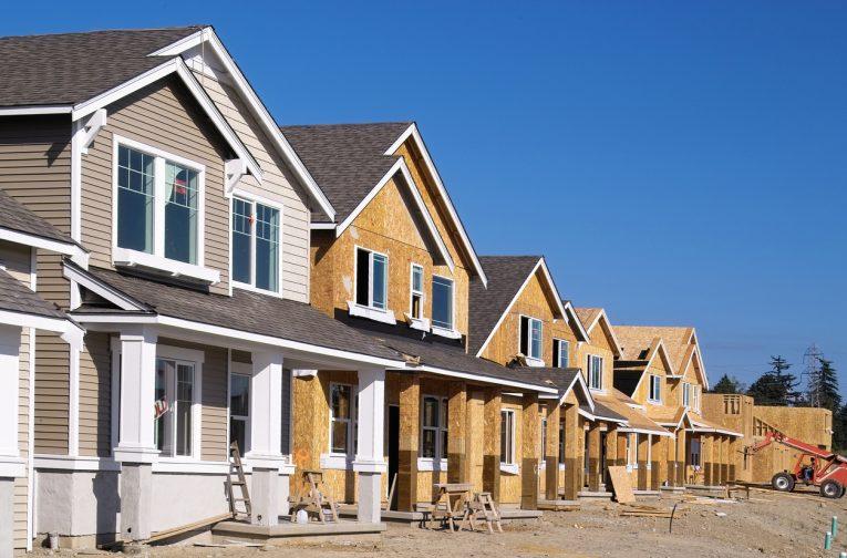 Perspective photo of a row of similar style houses during various phases of construction. should you buy a new or used home