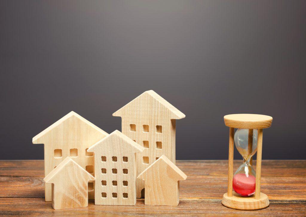 Wooden figures of houses and sand hourglass. Mortgage and loan concept, sell your home faster