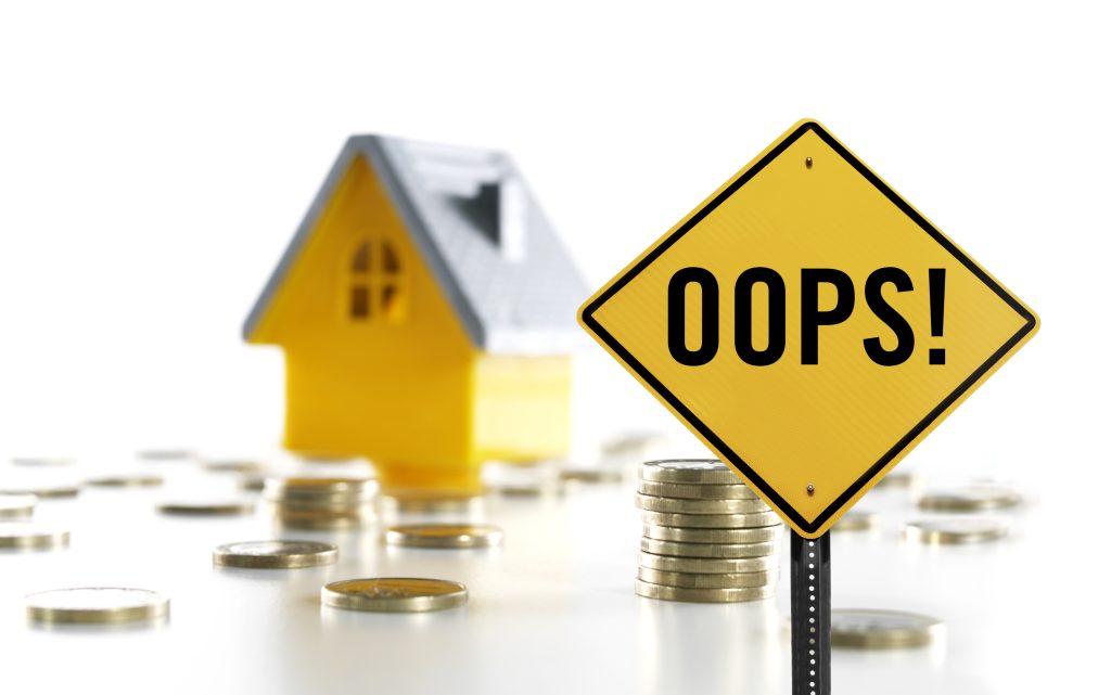 “OOPS!” traffic sign in front of a toy house and coins, concept first time house selling mistakes