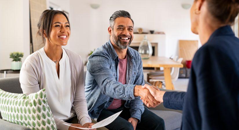 man shaking hands with financial advisor at home. Happy smiling couple greeting broker with handshake at home. Multiethnic mid adult man and hispanic woman sealing a contract to buy a house