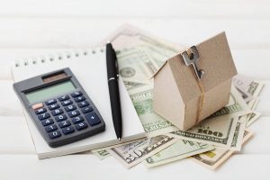Model of cardboard house with key, calculator, notebook, pen and cash dollars. House building, loan and real estate. Cost of public utilities, insurance, rent or buying a new home concept. mortgage
